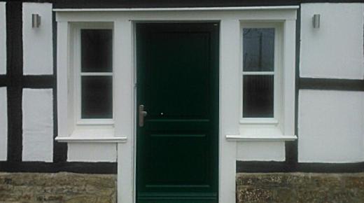 Holz-Haustür in dunkelgrün mit weißen Fenstern beidseitig